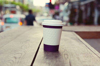 Paper coffee cup on wooden table over bokeh street
